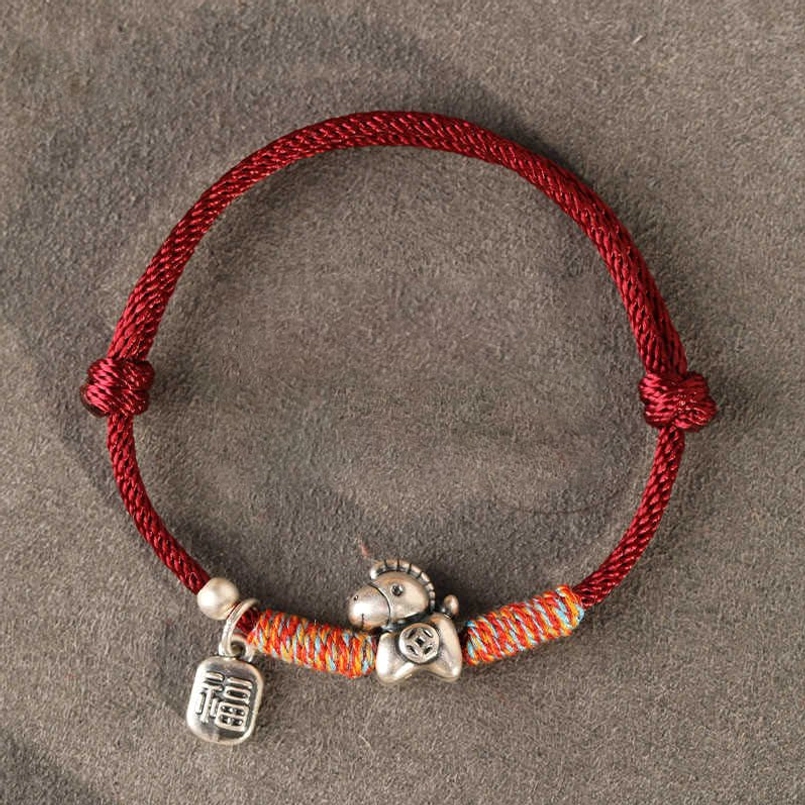 Dark red braided horse zodiac luck bracelet with engraved silver charms on grey velvet background