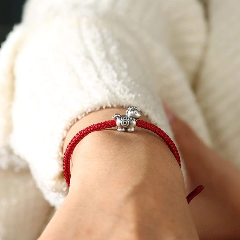 Adjustable red string bracelet with sterling silver horse charm worn on wrist close-up