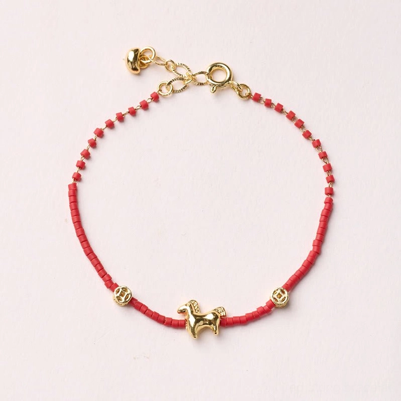 Adjustable red liuli glass horse bracelet with lobster clasp and extension chain displayed on pink background