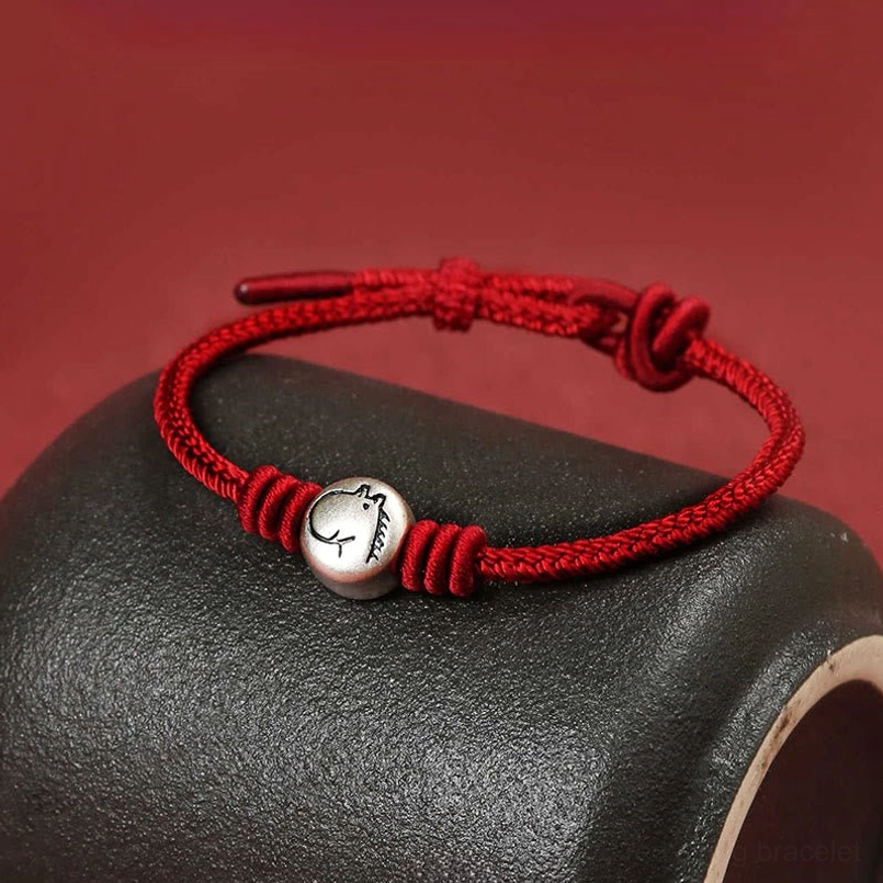 Horse zodiac braided red cord bracelet with vintage silver bead, angled side view on dark stone