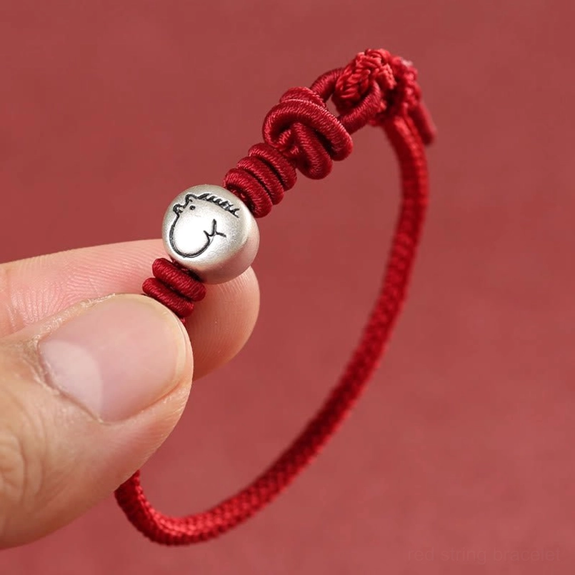 Close-up detail of sterling silver horse charm and braided red knots on wrist, hand-held view