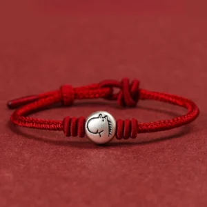 Year of the Horse red string bracelet with 999 sterling silver horse charm, flat lay view on red background