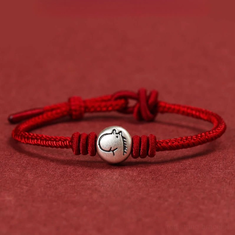 Year of the Horse red string bracelet with 999 sterling silver horse charm, flat lay view on red background