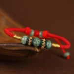 Jade abacus bead prosperity red string bracelet on wooden saucer dark background