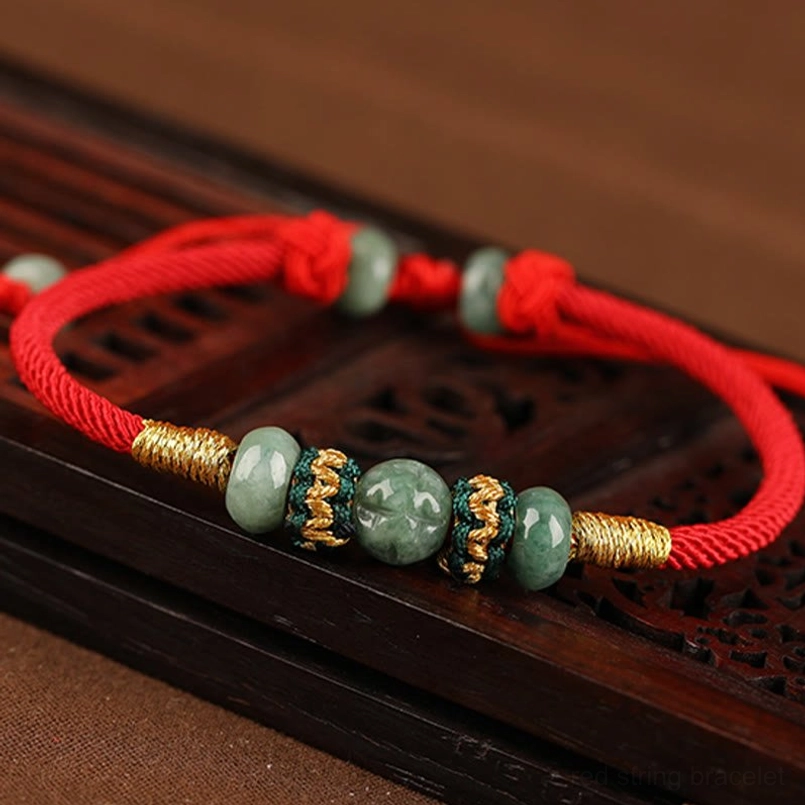 Jade red string bracelet side overhead view on carved dark wooden surface