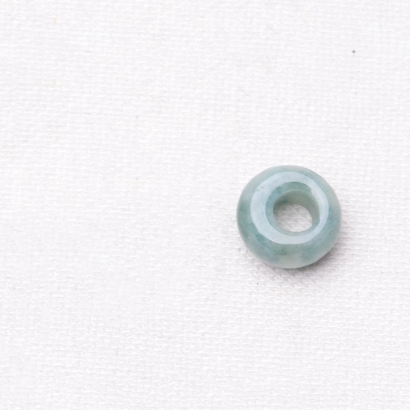 Single hollow light green jade bead circular ring glossy surface white fabric background