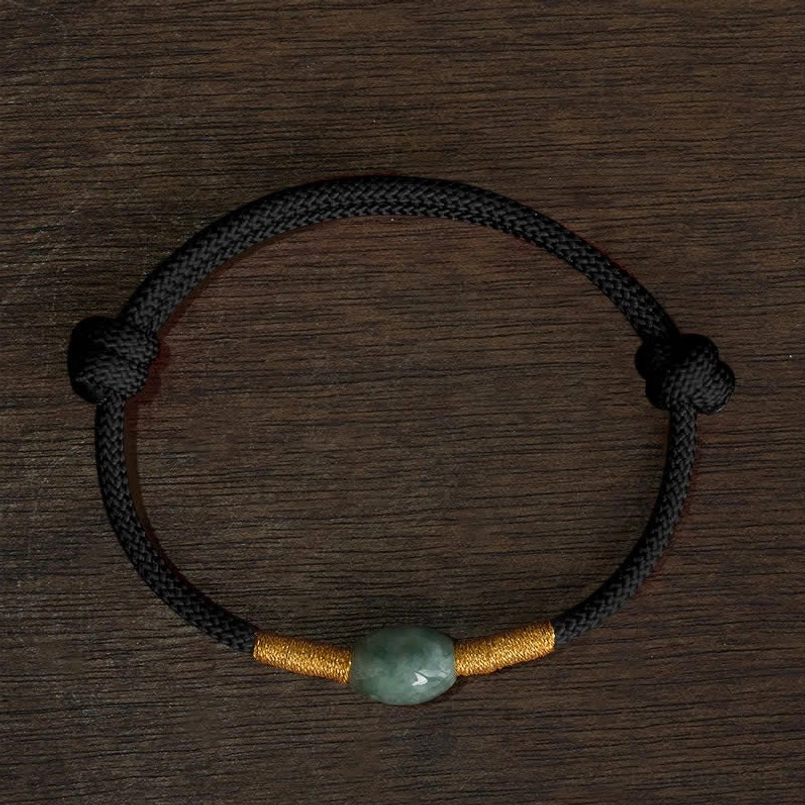 Black string jade bead bracelet with gold thread wraps wooden surface