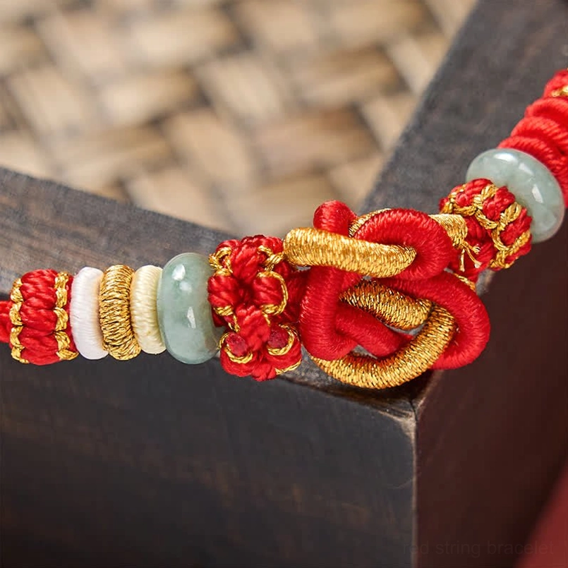 Macro view of red string jade bracelet showing heart knot and gold threading details
