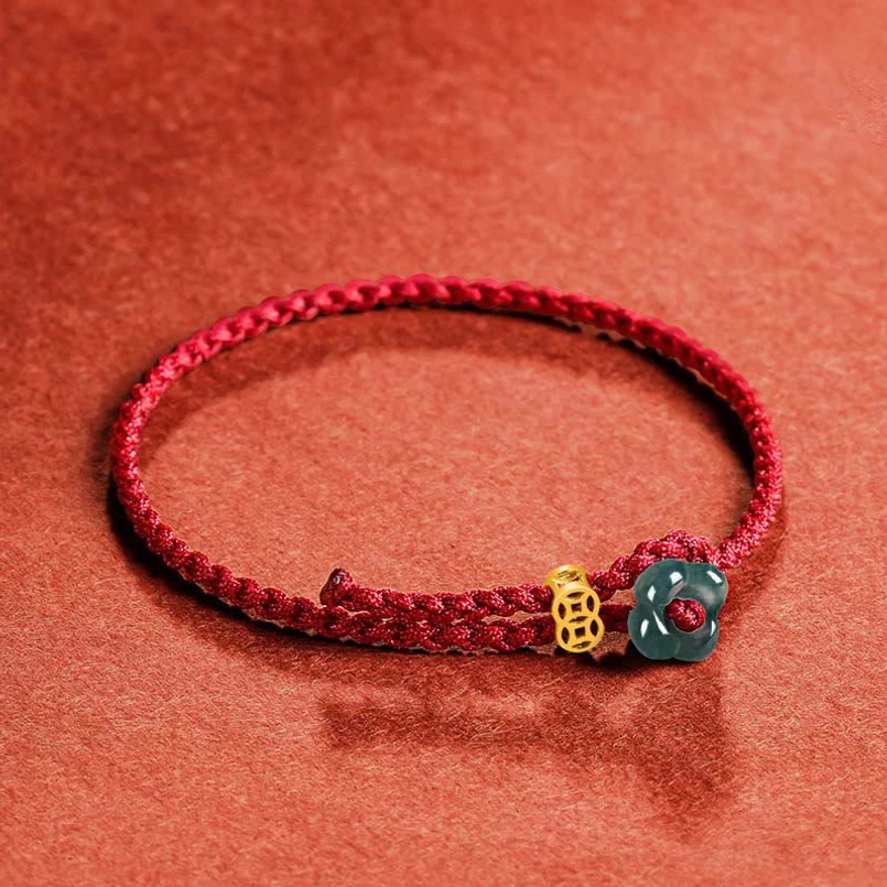 Red cord bracelet with jade flower and gold copper coin charm positioned on side