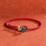 Jade flower and copper coin red string bracelet with braided cord on terracotta fabric background