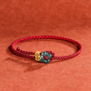 Jade flower and copper coin red string bracelet with braided cord on terracotta fabric background