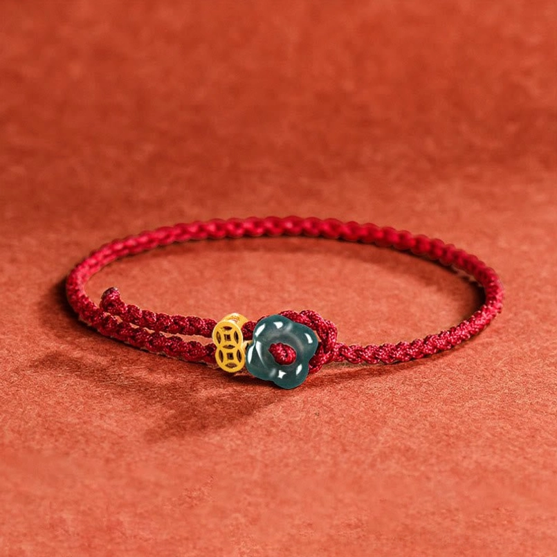 Jade flower and copper coin red string bracelet with braided cord on terracotta fabric background