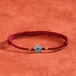 Jade flower red string blessing bracelet three quarter view on terracotta fabric