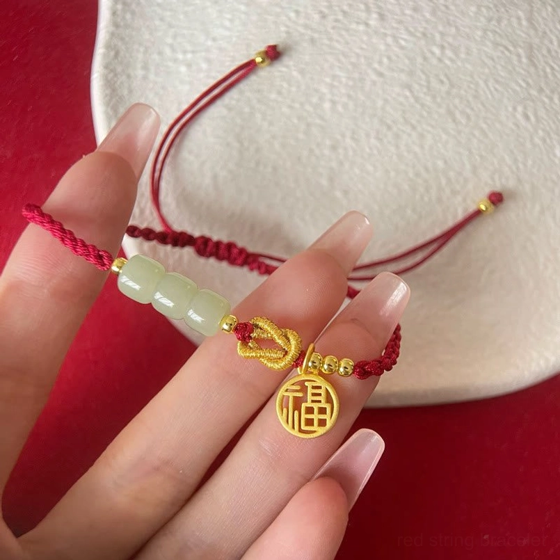 Close-up detail of jade beads and gold fu character charm on red braided cord