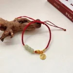 Handcrafted jade fu character red string bracelet with gold charm displayed on wooden surface with feng shui decor