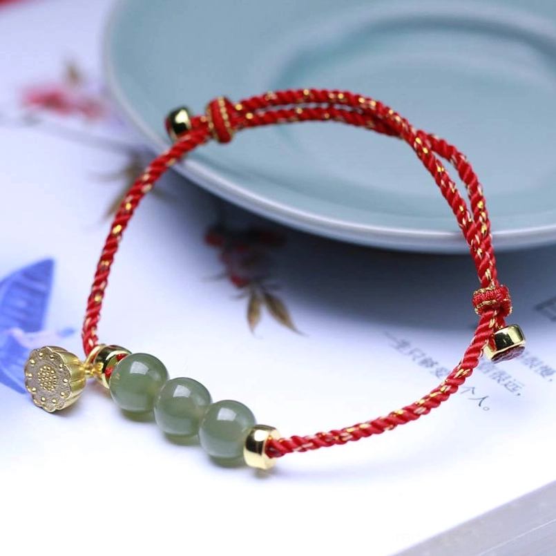 Red jade lotus string bracelet with gold charm and three light green jade beads on celadon background