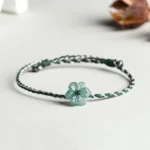 Side top view of jade orchid braided prosperity bracelet on minimalist light desktop