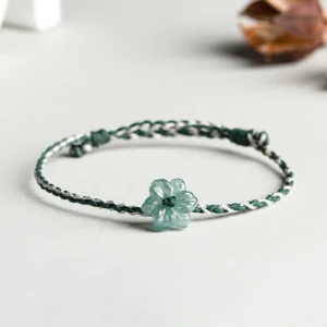 Side top view of jade orchid braided prosperity bracelet on minimalist light desktop
