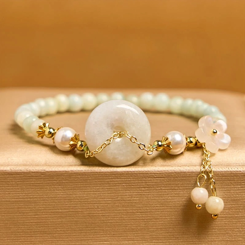 Flat lay jade peace buckle bracelet on wooden surface with floral charm and pearl accents