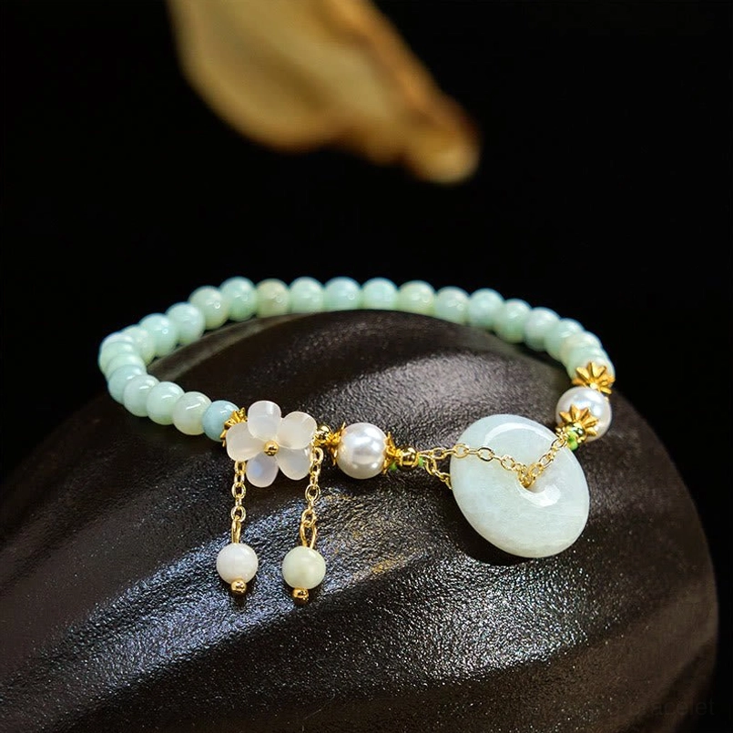 Jade peace buckle beaded bracelet with light jade beads and dangling pearl charms on dark stone