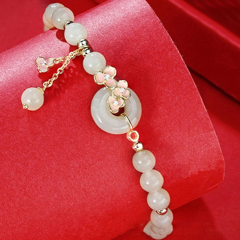 Single-strand hetian jade bracelet with gold-toned peace buckle and enamel flower charm on red velvet