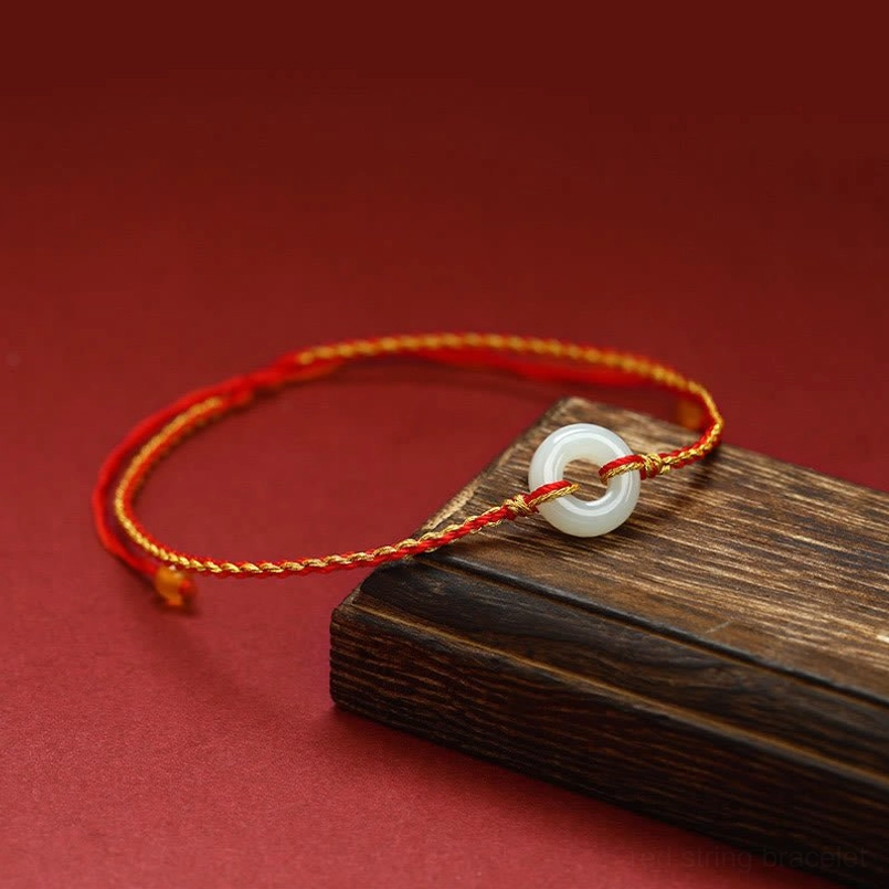 Jade peace buckle bracelet displayed on wooden block showing three-quarter view of braided red cord design