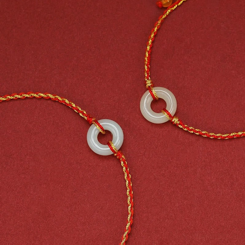Two handcrafted jade peace buckle bracelets with red-gold woven cords and white jade pendants overhead view