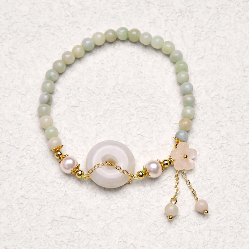 Full overhead flat lay of jade peace buckle bracelet with dangling floral and pearl charms