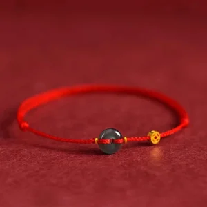 Jade peace buckle red string bracelet with gold copper coin charm on red fabric background - front flat view