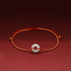 Jade peace buckle red string braided bracelet with gold-toned cord and white jade donut pendant on dark red background