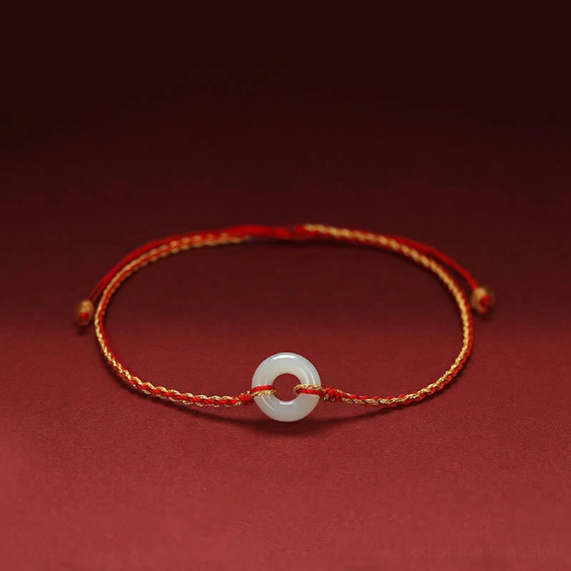 Jade peace buckle red string braided bracelet with gold-toned cord and white jade donut pendant on dark red background