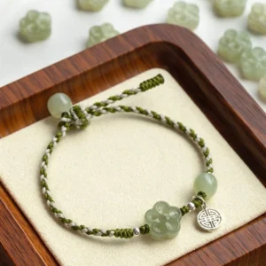 Handmade jade plum blossom prosperity bracelet with braided cord and silver charm on wooden display