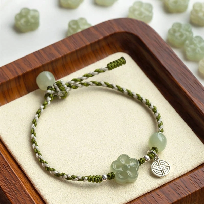 Handmade jade plum blossom prosperity bracelet with braided cord and silver charm on wooden display