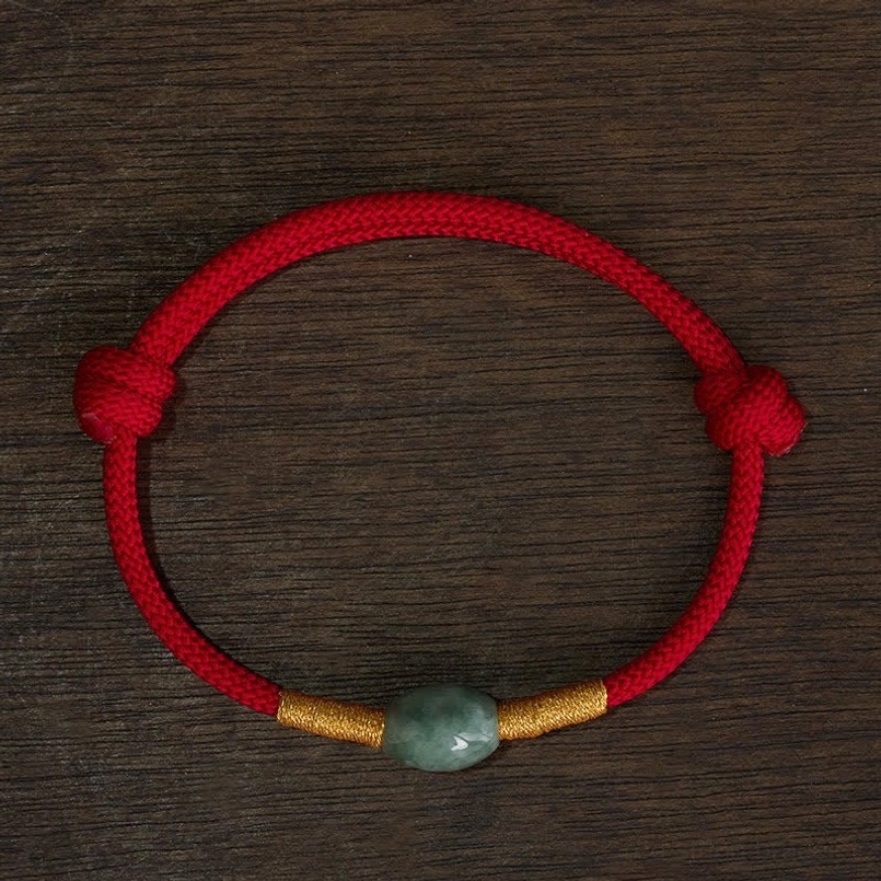 Red string jade bead bracelet with gold accents flat lay wooden background
