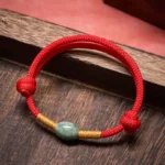Jade bead red string protection bracelet with gold accents on wooden surface