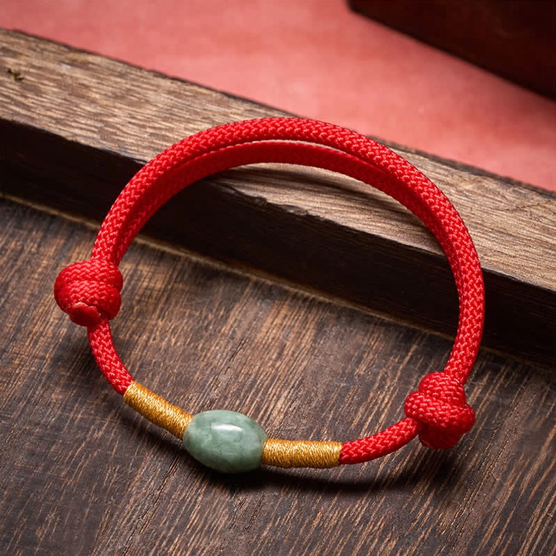 Jade bead red string protection bracelet with gold accents on wooden surface