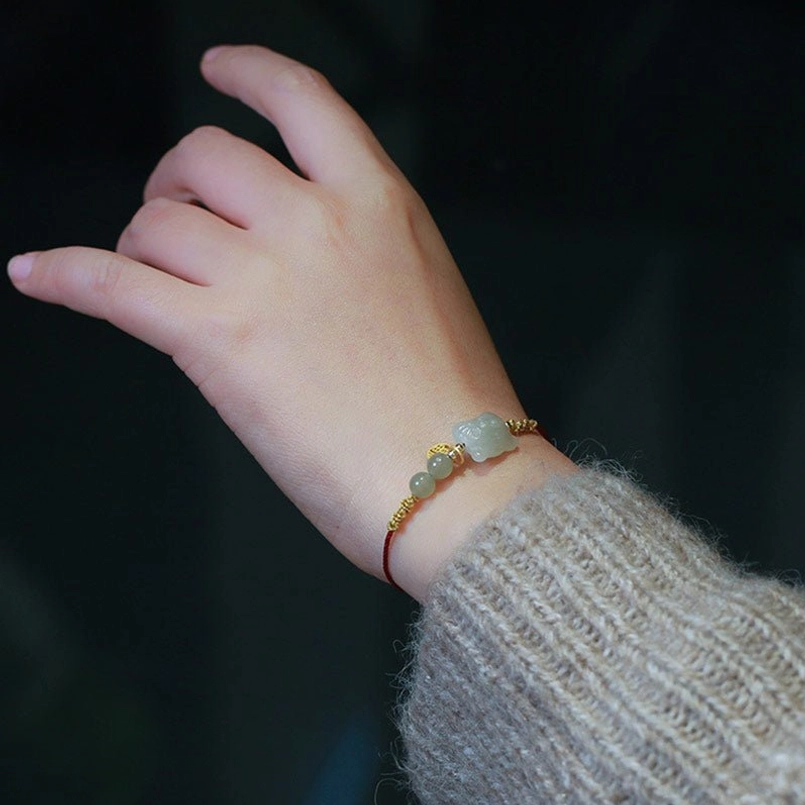 Minimalist jade beaded red string bracelet with thin red cord and gold chain accents on wrist