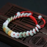 Red string jade bracelet with mixed color jade discs on wooden surface - top view