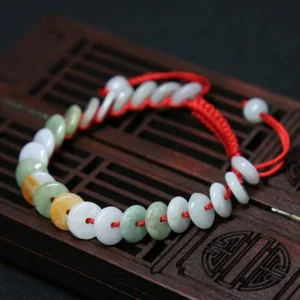 Red string jade bracelet with mixed color jade discs on wooden surface - top view