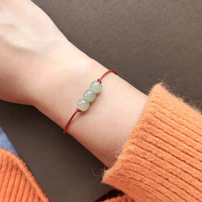Red string jade bracelet worn on wrist with orange sweater - casual daily wear styling