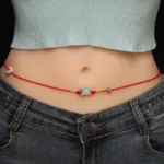 Red string belly chain with jade zodiac charm worn on waist over jeans - close-up waist shot