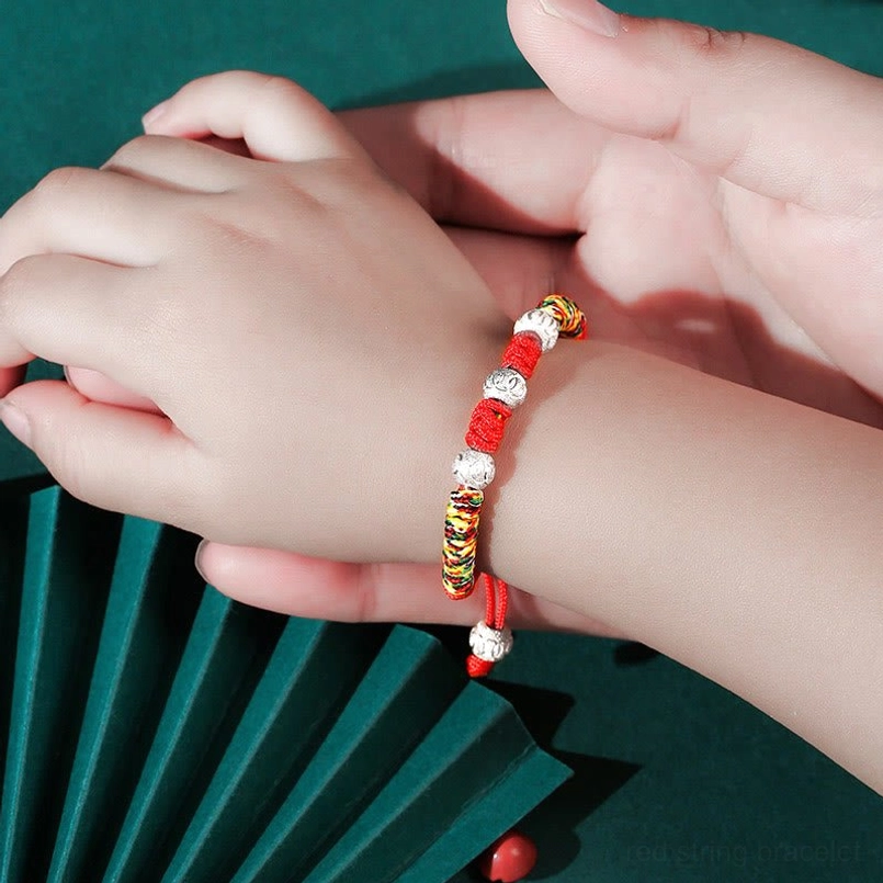 Child wearing red string King Kong knot bracelet on wrist with silver and colorful beads, close-up side view