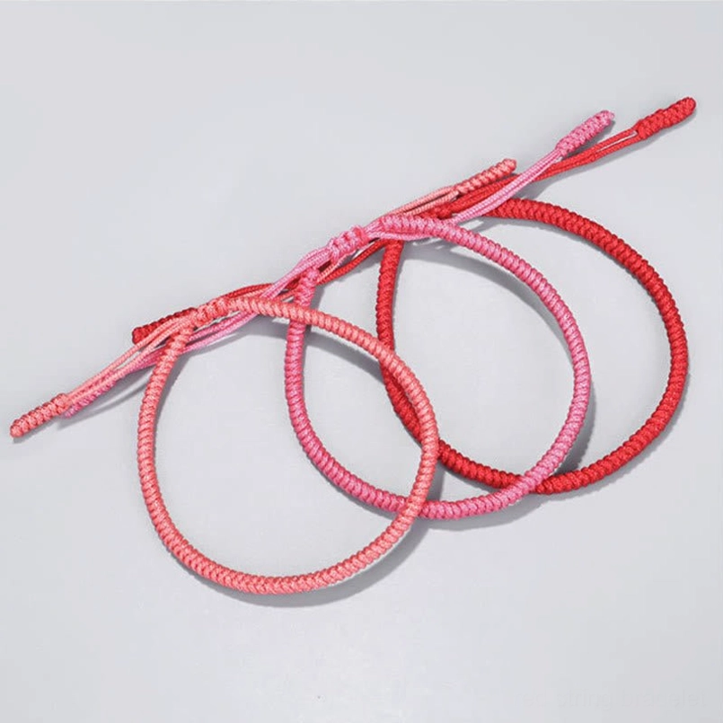 Soft light pink woven braided bracelet central knot design two tassel straps gray background