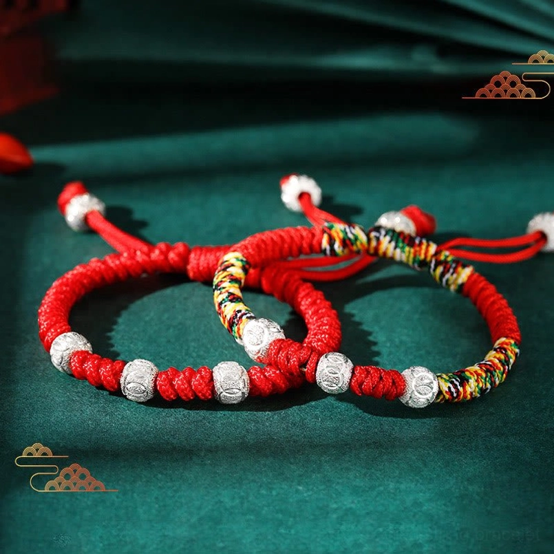 Kids King Kong knot red string bracelets with multicolor braided sections and 925 sterling silver beads on green tabletop