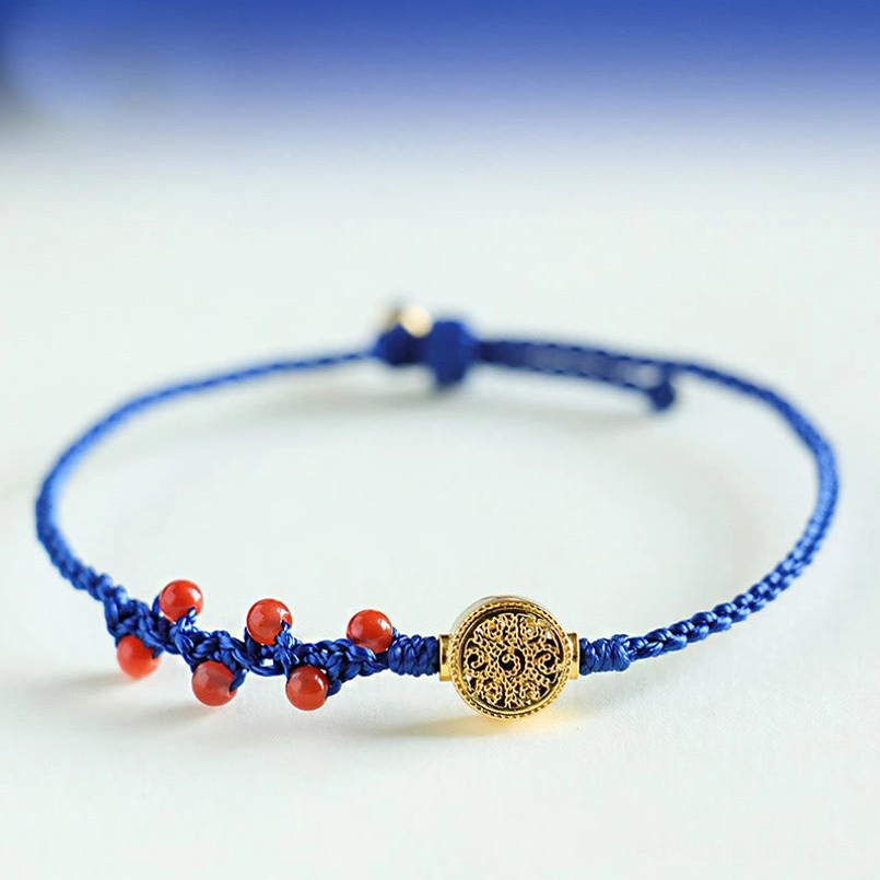 Klein blue string beaded bracelet with red gemstone beads engraved copper medallion flat lay on blue background