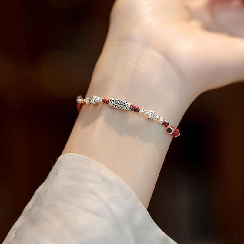 Red string koi fish bracelet worn on wrist showing side profile of silver charm and braided design
