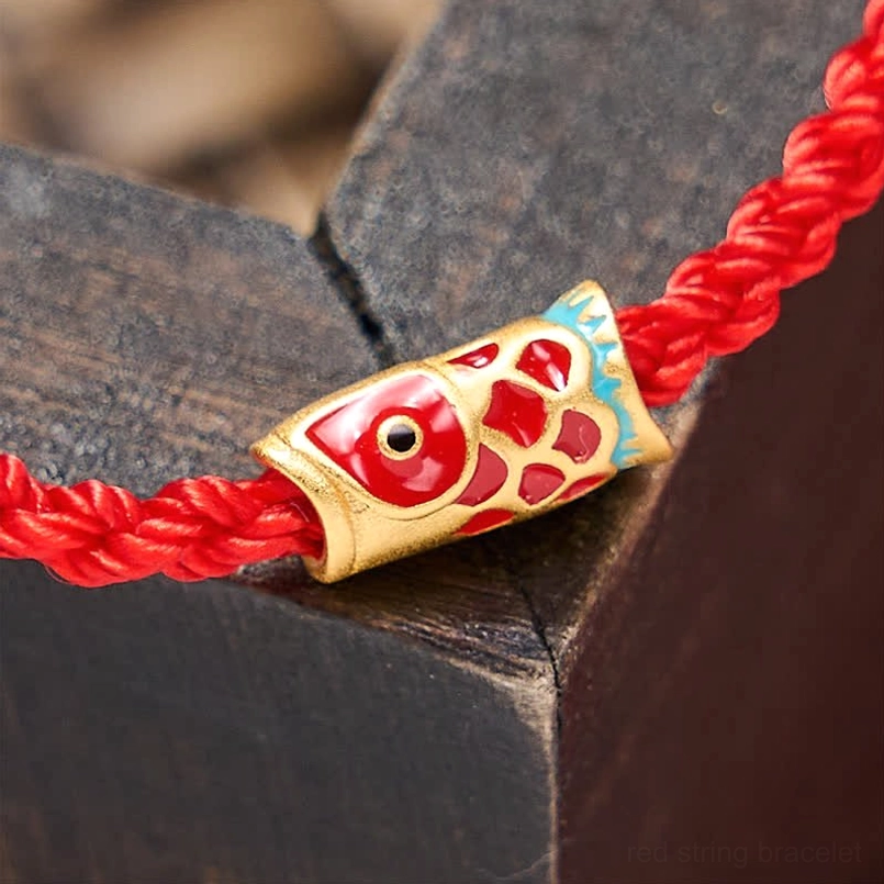 Enamel koi charm with red gold and blue accents on twisted red woven rope extreme close-up