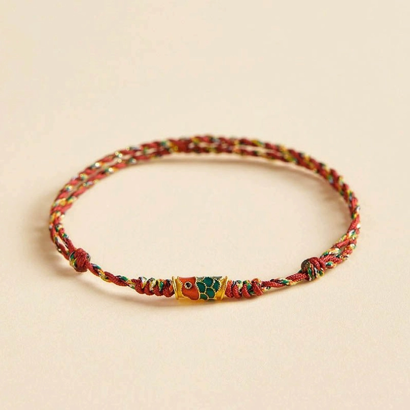 Angled view of multicolor red braided koi fish wealth bracelet with decorative enamel pendant