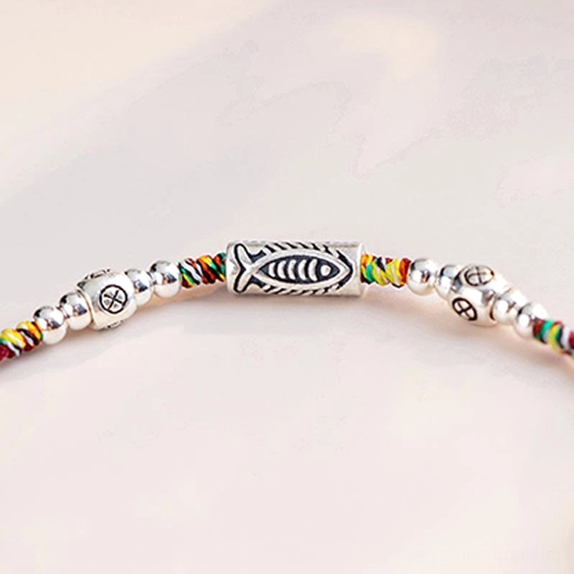 Close-up macro view of koi fish charm with round silver beads on red braided cord