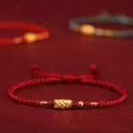 Close-up of 999 gold koi fish charm on red braided string bracelet
